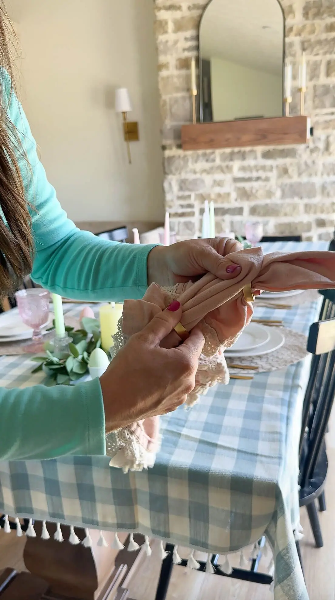 Close-up of hands styling a blush pink napkin with lace trim using a gold napkin ring for a spring tablescape.